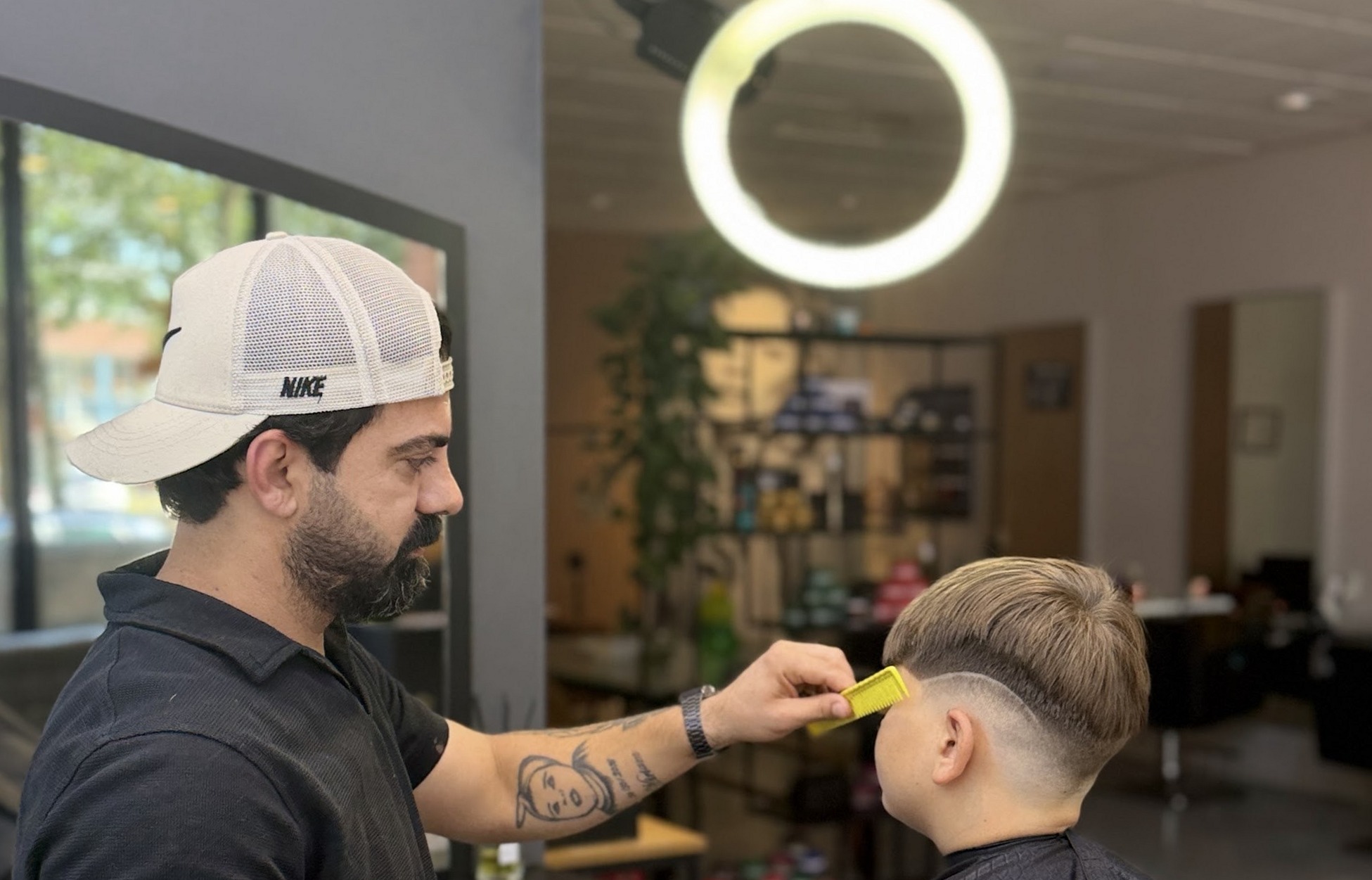 De kapper knipt een jongen in de stoel, met de ringlamp boven hen