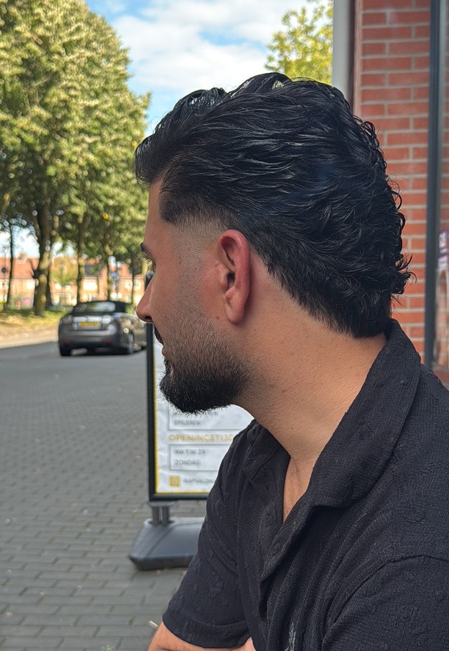 Een klant van opzij buiten de zaak, met krullen bovenop en een korte zijkant